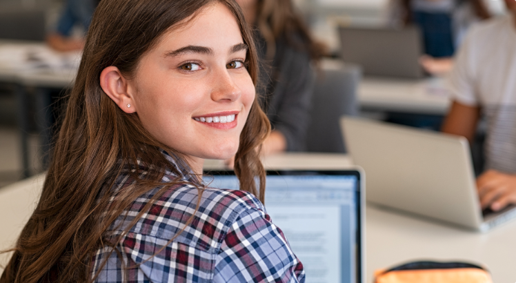 High school student on computer, looking at camera and smiling 