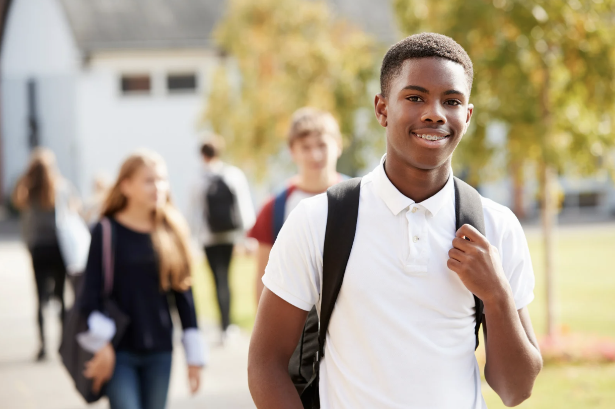 High school student boy smiling at camera with backpack on outside.